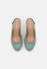 Světlé zelené slingback boty s hladkým semišovým povrchem, kulatou špičkou a světlým hnědým stélkou. Obsahují jemný výřezový design a nastavitelný pásek.