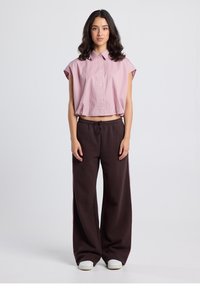 Maglietta a maniche corte a righe, ritagliata, in rosa chiaro e bianco; abbinata a pantaloni larghi marrone scuro e sneakers bianche.