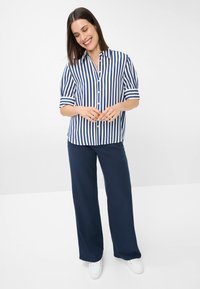 Camicia a righe blu e bianca a maniche corte con colletto, abbinata a pantaloni larghi blu e sneakers bianche.