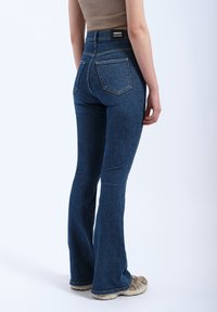 Fitted dark blue denim flared jeans with a high waist, five-pocket design, and a visible brand tag on the back waistband.