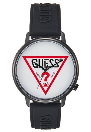 Runde schwarze Uhr mit weißem Zifferblatt, rotem dreieckigem Logo mit der Aufschrift „GUESS Washed Jeans“, schwarzem Silikonarmband mit geprägtem Markennamen.
