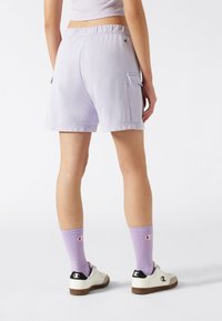 Pantaloni corti in cotone lilla con vestibilità rilassata, elastico in vita e tasche cargo laterali. Abbinati a calzini viola a costine e scarpe bianche.