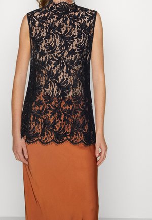 Ærmeløs sort blonder top med blomstermønster over en rustfarvet kjole, høj halsudskæring, bølget kant, båret af en stående person.