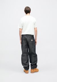 Ciemne spodnie dżinsowe o luźnym kroju, z dwoma tylnymi kieszeniami i żółtym przeszyciem. Noszone z białym t-shirtem i beżowymi butami.