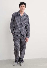 Conjunto de pijama de cuadros en azul marino, rojo y blanco; camisa de manga larga con botones y bolsillo, y pantalones a juego. Tejido suave y ligero con un ajuste relajado.