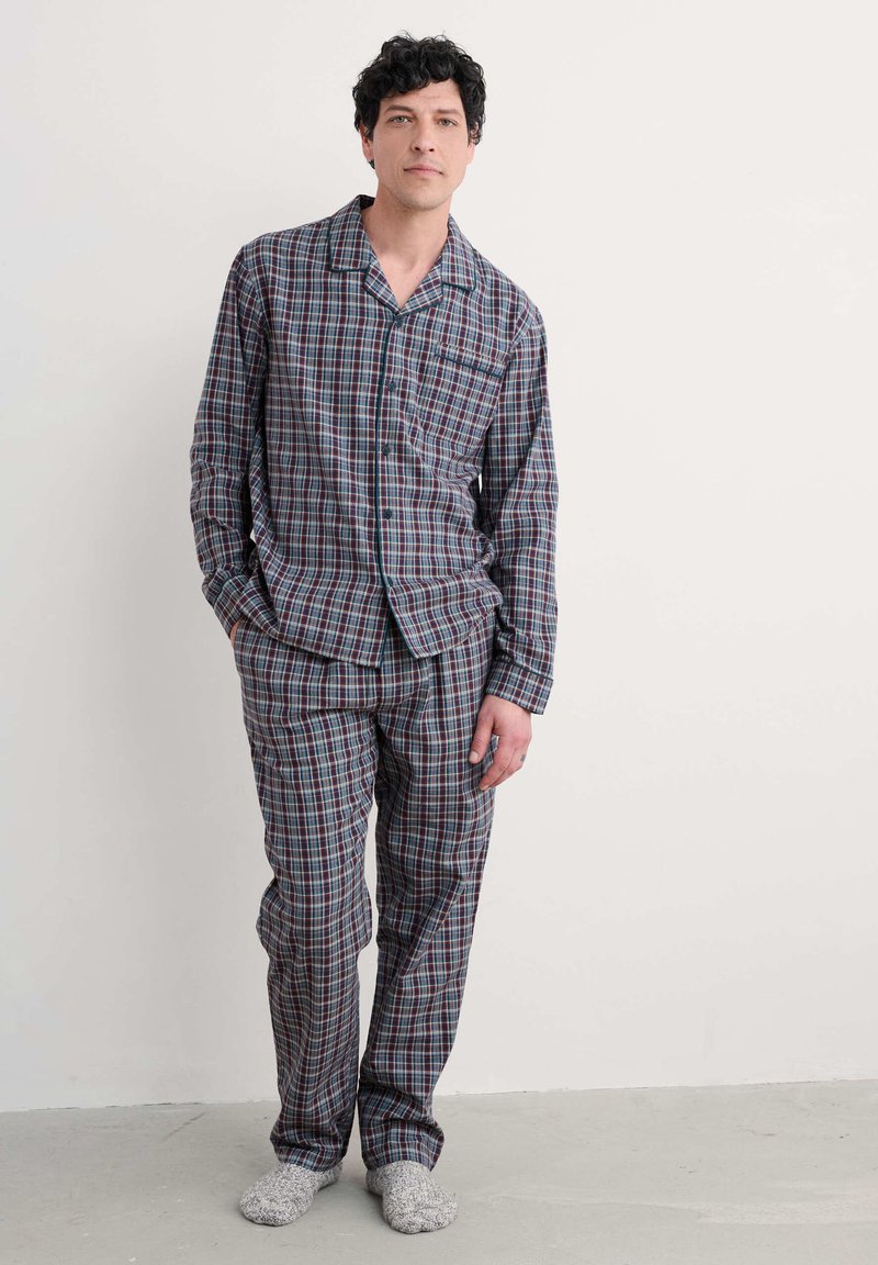Conjunto de pijama de cuadros en azul marino, rojo y blanco; camisa de manga larga con botones y bolsillo, y pantalones a juego. Tejido suave y ligero con un ajuste relajado.