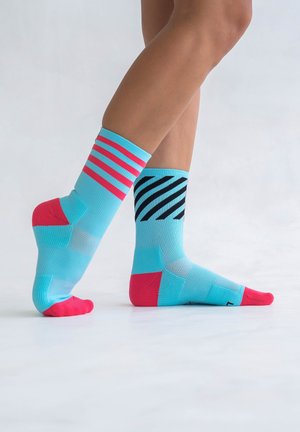 Helle blaue Socken mit rosa Akzenten. Eine Socke hat horizontale rosa Streifen, die andere diagonale schwarze Streifen. Strukturierte Oberfläche.