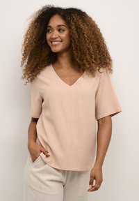 Ljust rosa kortärmad topp med V-ringning, tillverkad av en texturerad tyg, ihop med ljusa, avslappnade byxor.