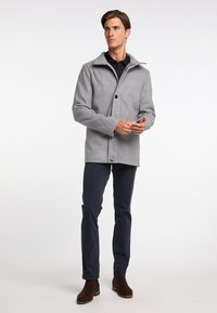 Jachetă gri din lână cu un guler structurat, închidere cu un singur nasture și buzunare laterale, purtată cu pantaloni bleumarin și botine din suede maro.