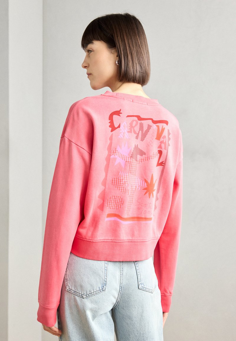 Sudadera corta rosa con un diseño gráfico en la parte posterior que presenta formas y patrones audaces. Puños y dobladillo acanalados. Tejido ligero.