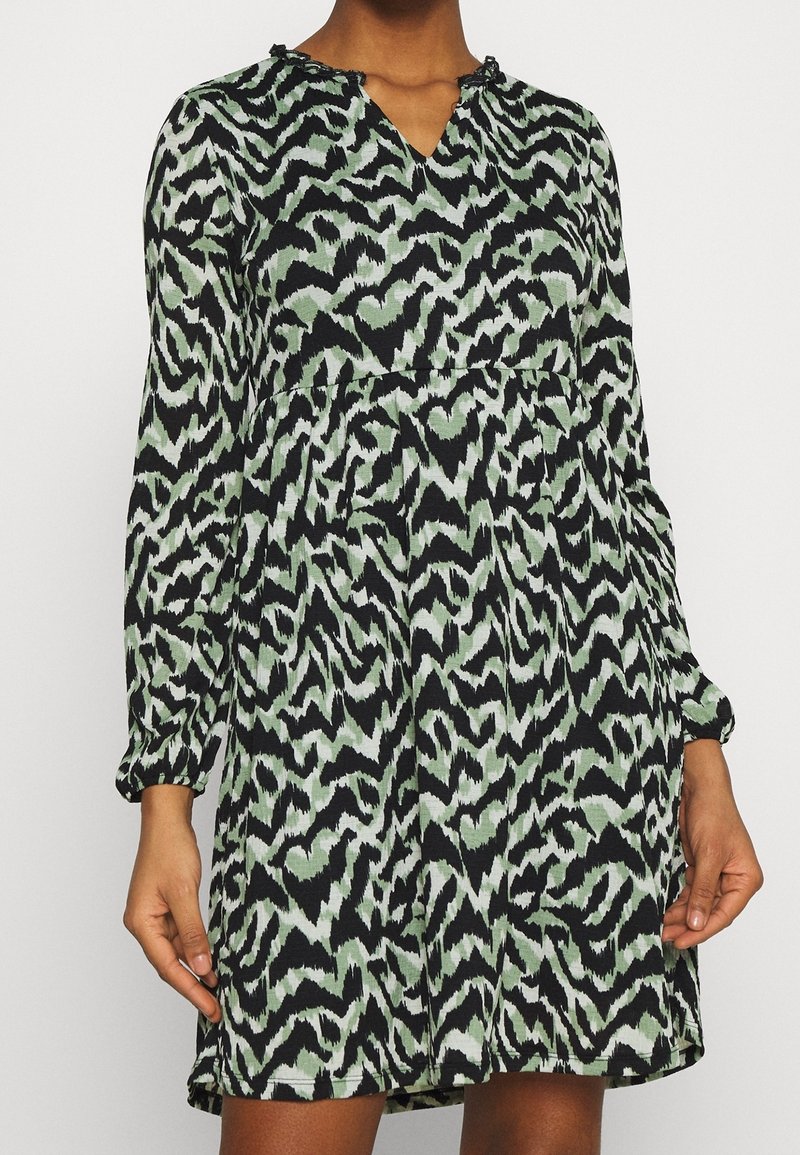 Langärmeliges Kleid in Schwarz und Grün, mit einem Zick-Zack-Muster, V-Ausschnitt und gefaltetem Oberteil, aus leichtem, strukturiertem Stoff.