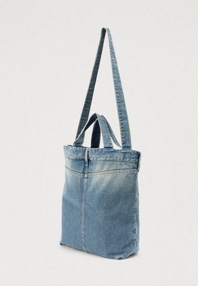 Džínsová taška na rameno s svetlomodrým prechodom farieb, dlhým ramenným popruhom, krátkymi hornými rúčkami a zapínaním na zips. Má jednoduchú, hladkú textúru.
