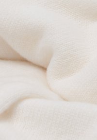 Mjukt krämfärgat tyg med en fin, stickad struktur. Materialet ser lätt och något fluffigt ut, med synligt söm mönster.