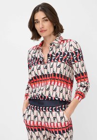 Camicia a maniche lunghe con bottoni caratterizzata da un motivo geometrico in rosso, rosa e blu navy. Tessuto morbido con colletto classico e polsini con bottoni.