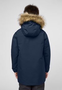 Námořnická modrá parka s kapucí podloženou umělou kožešinou. Má jednoduchý, štíhlý design s elastickými manžetami a střední délkou pro teplo.