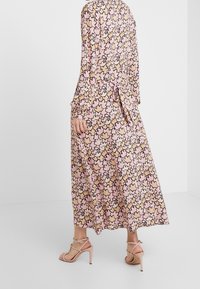 Lång klänning med blommönster på rosa botten och svart-beigea bladmotiv. Mjuk tygkvalitet med långa ärmar och knytbar midjedetalj.