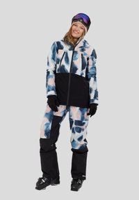 Skikleding met een patroon op de jas in blauw, wit en roze met zwarte accenten, gecombineerd met bijpassende broek en zwarte handschoenen.