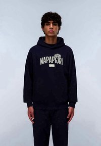 Hoodie azul escuro com um logótipo à frente, feito de tecido macio, com um bolso canguru e punhos em canelado. Usado com calças escuras combinando.