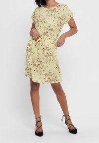 Robe à manches courtes à fleurs en tissu jaune pastel, cintrée à la taille avec une ceinture, dotée d'une jupe fluide et de motifs floraux subtils.