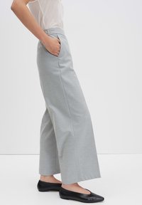 Grijze wijde broek met zijknopen, gemaakt van een gestructureerde stof. Gecombineerd met zwarte flats en een licht, doorschijnend topje.