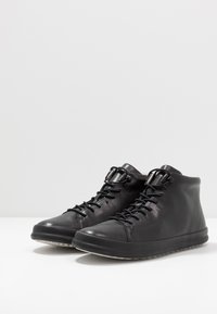 Black leather high-top shoes with lace closure, rounded toe, and rubber sole. Features a minimal design and smooth texture.