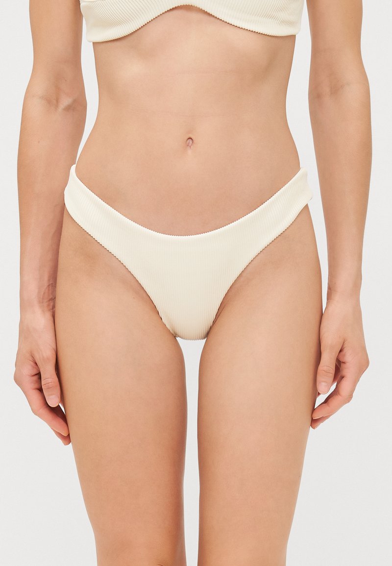 Kremveida ribota bikini apakšda ar augstu griezumu un gludu tekstūru. Izceļas ar zemu jostasvietu un minimālu pārklājumu, uzsverot elegantu siluetu.