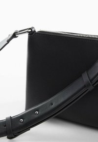 Sort læder crossbody taske med sølv lynlås og justerbar stropp med metalspænde og huller på en hvid baggrund.