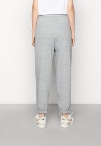 Grå sweatpants med en texturerad tyg, elastisk midja och smalnande anklar, bärs med vita sneakers med ljusguldiga detaljer.