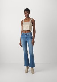 Beige avkortet topp med firkantet halslinje, paired med lyseblå vide jeans. Modell med nude hæl boots. Glatt stoff med subtil glans.