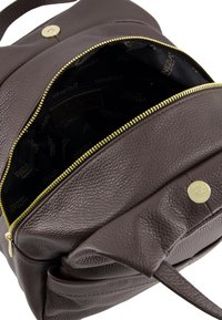 Brown leather backpack with a textured finish, featuring a gold zipper and snap closure. Interior is black with brand logo.