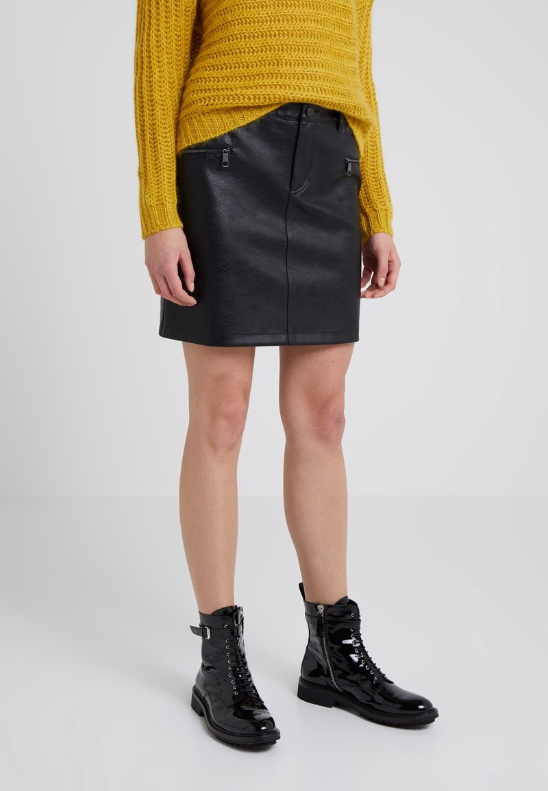 Czarna skórzana mini spódnica z zamkiem z przodu i dwoma kieszeniami na zamek błyskawiczny, połączona z żółtym swetrem z teksturowanego dzianiny i czarnymi lakierowanymi botkami na sznurówki.