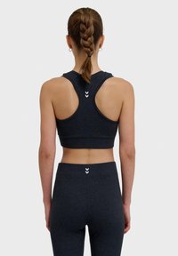 Mörkgrå atletisk crop top med racerspannée-design, tillverkad av en slät tyg, med vita accenter och en figurnära silhuett. Matchad med leggings.