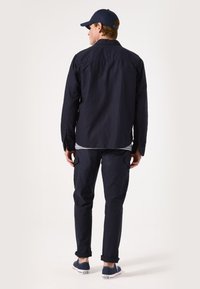 Marineblauwe overhemd met lange mouwen, ontspannen pasvorm, gecombineerd met marineblauwe cargobroek met zijzakken en marineblauwe canvas schoenen.