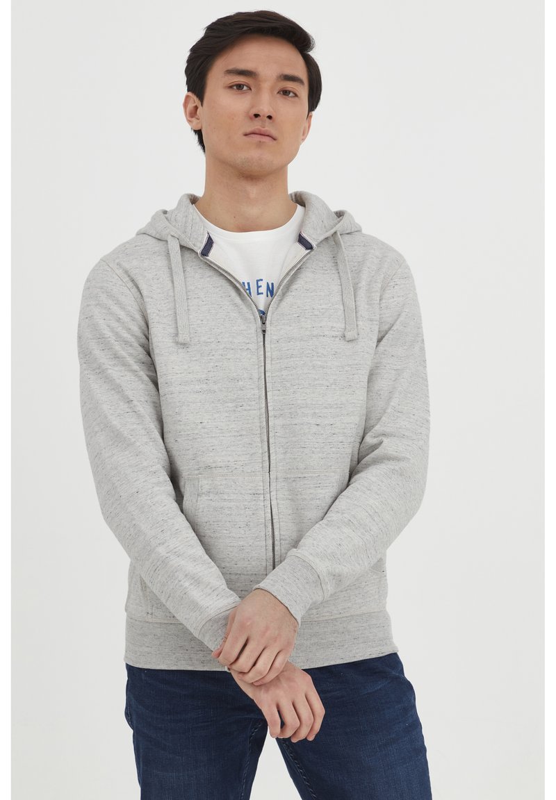 Grå hettegenser med glidelås og teksturert overflate, snorhette og lommer foran. Kombinert med en hvit t-skjorte og blå jeans.