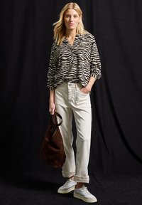 Svartvit zebra-randig blus, gräddfärgade baggy-byxor, grå sneakers och en brun mockaväska. Platt textur och avslappnad passform.