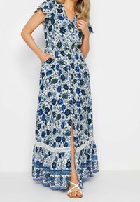 Blommig maxiklänning i vitt och blått, med korta volangärmar, V-ringning, framknappering, fickor och en flerlagrad nederkant med spetsdetaljer.