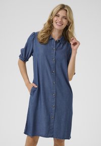Rochie din denim cu mâneci bufante scurte, închidere cu nasturi în față și buzunare laterale. Are o croială lejeră și un tiv până la genunchi, de culoare albastru solid.