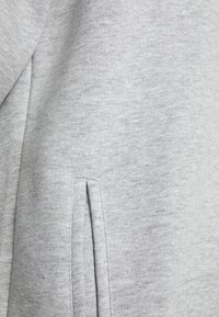 Tejido de sudadera gris con una textura suave, que presenta un bolsillo lateral y una apariencia ligeramente jaspeada. Diseño sencillo y casual.