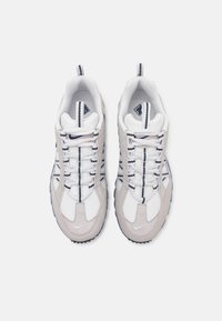 Vita och ljusgrå sneakers med ett texturerat tygovandel, utrustade med svarta och grå skosnören samt en gummiyttersula med greppdetaljer.