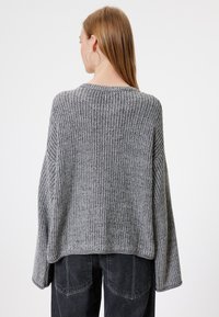 Grauer, gestrickter Pullover mit lockerem Schnitt, weiten Ärmeln und gerippter Textur. Der Saum ist leicht cropped und ergänzt eine dunkle Jeans.