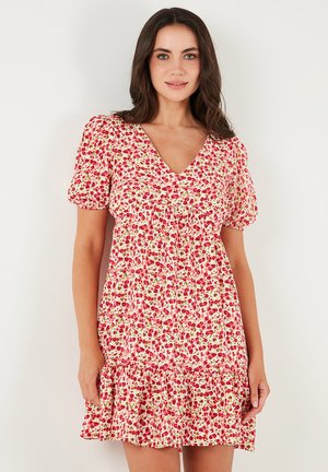 Short floral dress in white with red and green patterns, v-neckline, puff sleeves, and a tiered ruffle hem. Lightweight fabric.