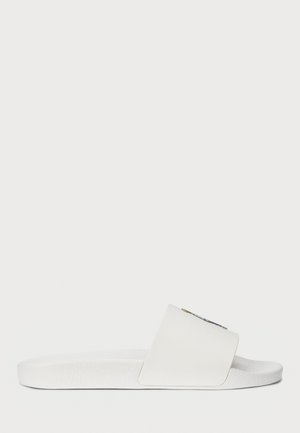 White slide sandal with a wide strap and textured footbed. Features a decorative element on the strap, smooth material, and minimalist design.
