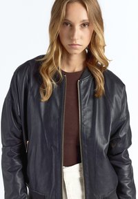 Sort læder bomberjakke med lynlås foran, ribstrikket krave og sidelommer. Glat tekstur og afslappet pasform.