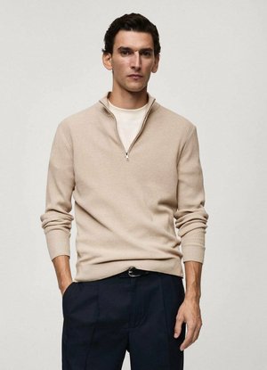 Maglione beige a coste con colletto zip, slim fit, maniche lunghe. Indossato sopra una camicia chiara, abbinato a pantaloni scuri. Design semplice.