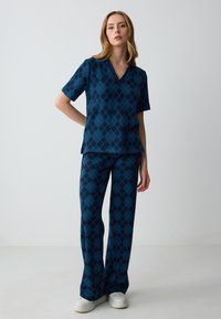 Maglia a maniche corte e scollo a V con pantaloni abbinati in blu scuro, decorati con un motivo a diamante in tonalità più chiare di blu e verde, realizzati in tessuto morbido.