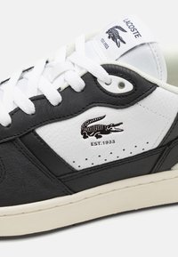 Fekete-fehér bőrsneaker, texturált fekete panelekkel, sima fehér kiegészítésekkel, hímzett logóval és fehér fűzőkkel. Vintage stílusú.