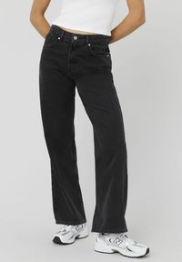 Jean droit noir en denim, avec une taille haute, un design classique à cinq poches et des détails de couture subtils.