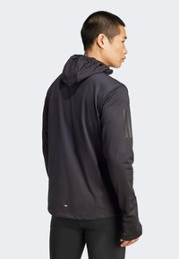 Schwarzes sportliches Hoodie mit taillierter Passform, strukturiertem Stoff und verstellbarem Kapuzenzug. Mit einem Logo auf dem linken Ärmel.