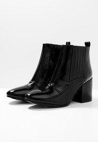 Botines negros con un acabado patent brillante, punta cuadrada, paneles laterales acanalados y un tacón grueso para mayor altura y soporte.