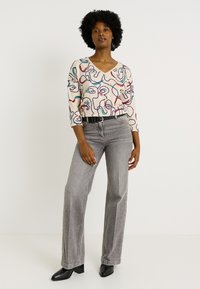 Pull à col en V avec des motifs abstraits multicolores, associé à un jean large gris. Des bottines à talons noires complètent l'ensemble.